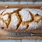"Traditioneller Dresdner Stollen Rezept auf Holzbrett mit Puderzucker, Marzipanfüllung und festlichen Dekorationselementen wie Tannenzweig und Zimtstange.